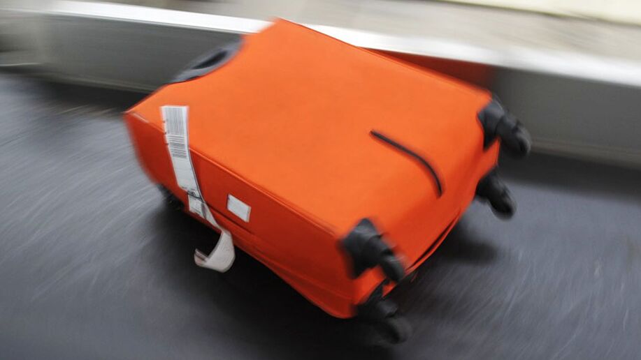 Orangener Koffer auf einem Gepäckförderband