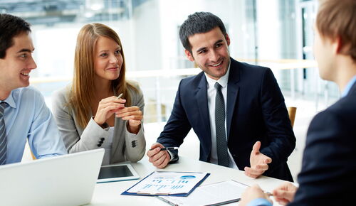 Four young professionals are sitting at an office table and discussing business topics